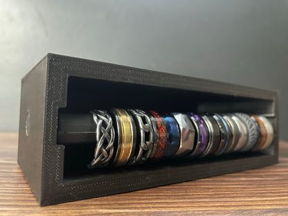 Black Cowan Cases ring case with slide-out ring bar extended, holding many rings, angled view