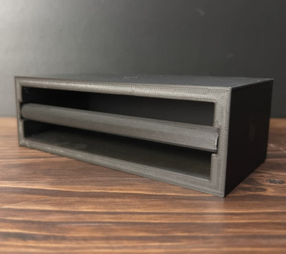 A black modular ring case with a slide-out ring bar, placed on a wooden surface.