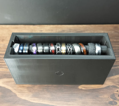 Black Cowan Cases ring case with slide-out ring bar filled with rings, face-up view from above